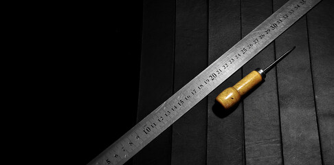 Metal measuring ruler and awl on leather base. Dark background. Minimal artificial lighting. Copy space