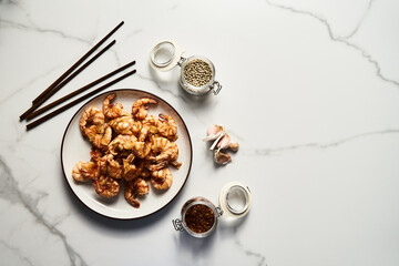 Crispy Pan fried tiger shrimps or prawns with garlic. Chinese or Asian cuisine dish. Shrimps lay on white plate on white marble background. Top view food photo.