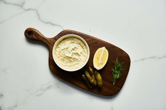 Classic Tartar Sauce dip in the bowl on wood board. Mayonnaise with dill and capers plus lemon, shallot onion. Worcester sauce and Dijon Mustard. 