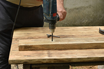 The carpenter works with a drill drills a hole.