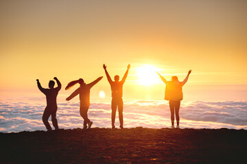 Group of happy tourists are having fun and dance at sunrise on mountain top over clouds