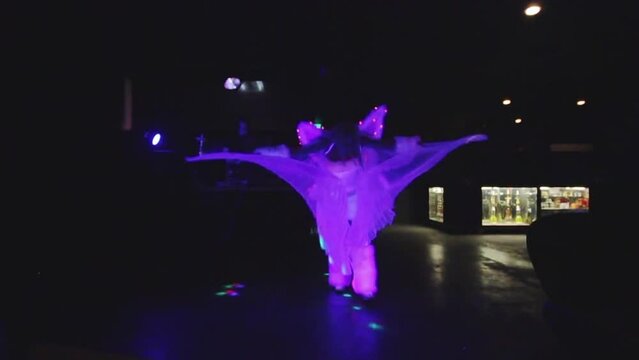 Professional female dancer performing in white phosphorus costume with wings at night, slow motion