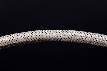 Close-up of a metal hose, with crisscrossed silver strands, isolated on black background.