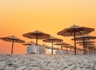 Straw umbrellas with sunbeds on the beach. Straw umbrellas and stacked deck chairs on the beach at...