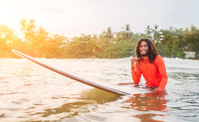 Black long-haired teen man showing shaka sign floating on long surfboard, waiting wave ready...