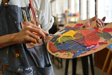 Close-up image of a young creative artist's hands smeared with watercolors holding a spatula mixing...