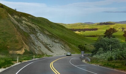 Scenic landscape featuring a winding road with two yellow lines, bordered by a lush green hillside.