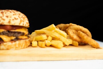 Burger, golden french fries, and onion rings presented on a wooden cutting board.