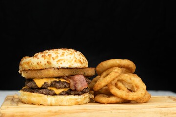 Freshly-prepared cheeseburger with fried onion rings served on a wooden cutting board.