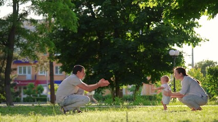 baby first steps parents. the kid took his first steps in the park next to his parents family. baby happiness on the faces of adults. waiting for the lifestyle first step from the child