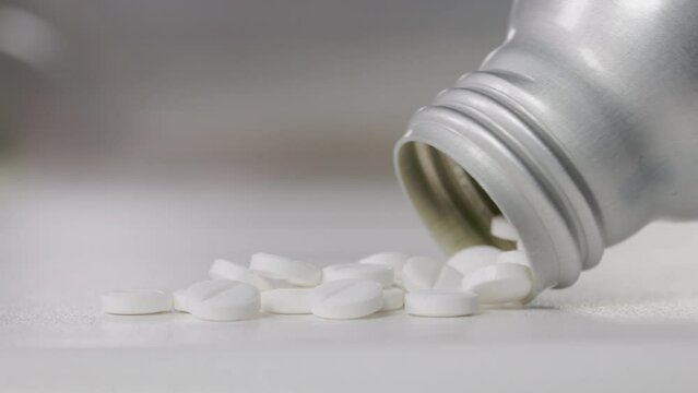 Closeup shot of white pills spilling out of a silver bottle on a table
