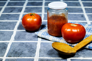 tomato sauce in glass bottle with wooden spoon on tile floor