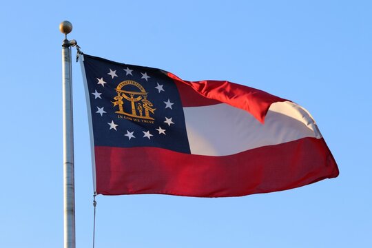 Closeup of a Georgia state flag flying on flagpole under the blue sky