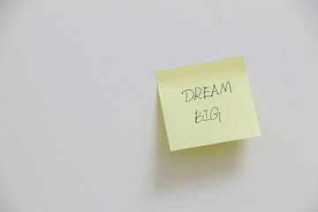 Motivational and inspirational message to dream big on yellow sticky note on white wall, ambition concept for work and life
