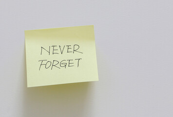 Yellow sticky note stuck on white wall with a reminder to never forget, memory concept