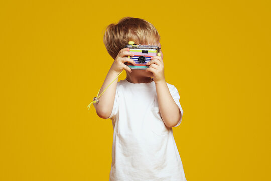 Little kid with blonde hair holding camera in hands and taking picture, aiming at camera.