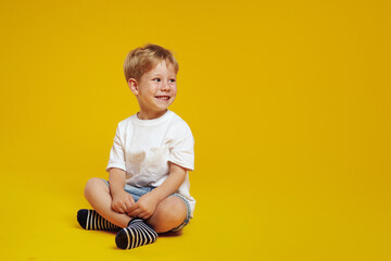 Joyful little boy smiling and looking at free empty space for text while sitting cross legged.