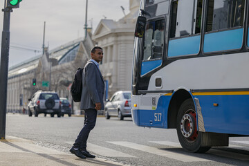 Latino man with formal ware and backpack crossing the street in a city.