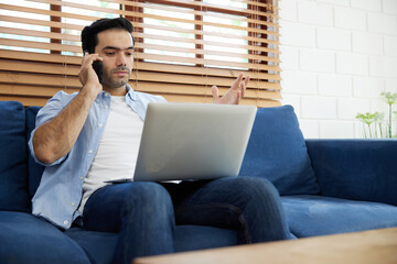 young handsome man using laptop computer and talking by smartphone at home