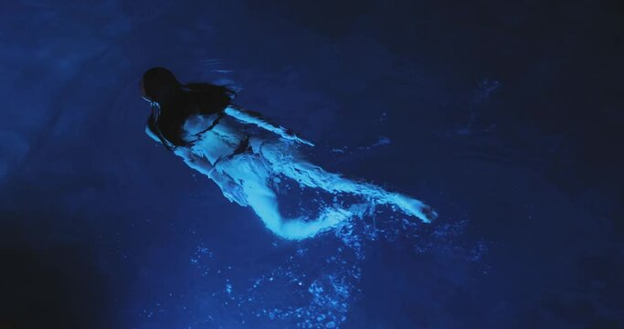 Calm beautiful young woman relaxing in a luxury swimming pool at night, view from above. High-quality photo