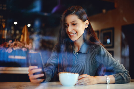 Attractive woman in a coffee shop using smartphone while drinking coffee at cafe