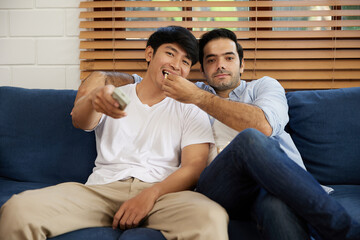 LGBT gay couple watching tv and eating popcorn in living room