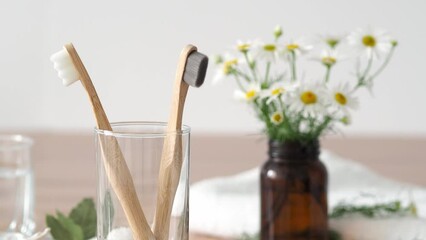still life with flowers. A woman takes a wooden toothbrush from a glass in the bathroom. Bamboo toothbrushes with soft bristles. Morning care. Zero waste concept. Eco-friendly bamboo toothbrushes.