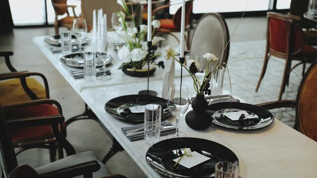 Wedding decor, all decorated in black and white colors, dolly shot of festive decorated table. Beautiful black plates with tender flower on it, candles.
