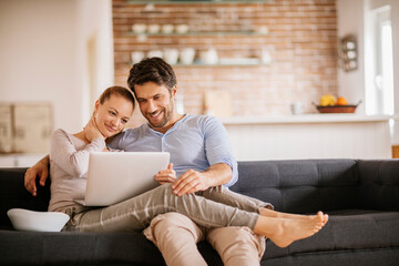 Young couple using a laptop on the couch in the living room at home