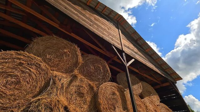 Straw hay roll stacked at barn wooden countryside roof storage with blue sky clouds rural panorama