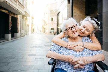 Senior woman embracing her mother who is in a wheelchair. Senior woman taking care of her mother...