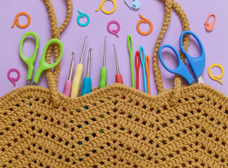 Yellow crochet bag with bright crochet tools on a purple backgrond. Top view.