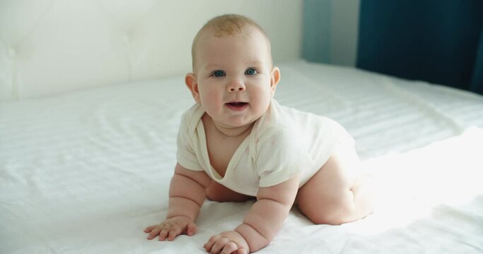little cute european baby crawls on all fours on the bed in the room. High quality 4k footage