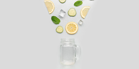 Mason jar with ingredients for preparing cold cucumber lemonade on light background