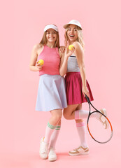 Young sisters with tennis racket and balls on pink background