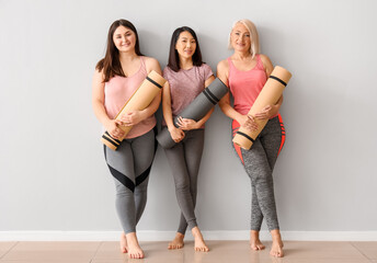 Sporty women with fitness mats near light wall