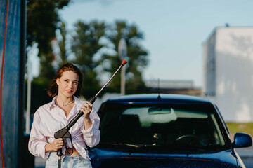 Beautiful woman at the car wash washes the car.