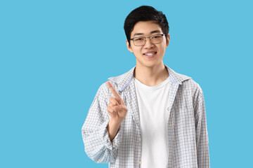 Young Asian man pointing at something on blue background