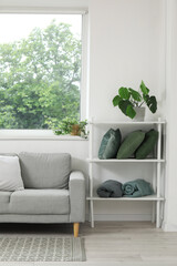 Stylish grey sofa, shelving unit with pillows and houseplants near window in living room
