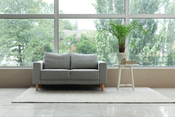 Stylish grey sofa and table with houseplant near window in living room