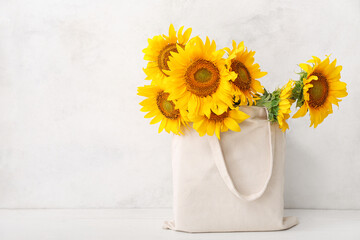 Eco bag with beautiful sunflowers on white wooden table