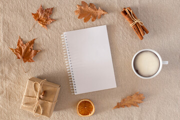 Autumn composition with an empty diary, a cup of coffee, autumn dry leaves, a gift wrapped in craft paper on a linen fabric background. Flat lay, copy space, Autumn, fall concept.