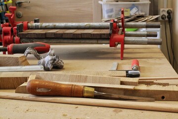 Craft carpentry workshop with variety of wooden pieces and planks, hand tools and wooden work bench in the foreground. Joinery with workbench and lots of wood. Carpenters table with furniture details