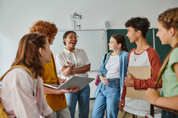 happy african american teacher talking to teenage students in classroom, back to school concept