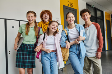 Obraz premium teenage schoolkids looking at camera and standing in school hallway, teen classmates with devices
