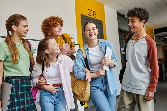 teenage schoolkids laughing and standing in school hallway together, teen classmates with devices