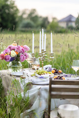Summer sunset, romantic date outdoors in meadow, marriage proposal. Romantic sunset dinner in the field. Table honeymoon set for two with luxurious food, glasses of champagne drinks in a restaurant.