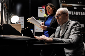 Business employees brainstorming accountancy data analysis report using laptop and statistics document records. Archive file room filled with cabinet, folders and flowcharts