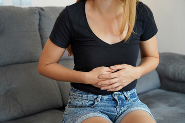 Digestive problems from poor diet. Young woman suffering from strong abdominal pain while sitting...