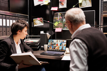 Private detectives having online videocall with remote team, discussing mysterious suspect report, working late at night at criminal case in arhive room. Meeting conference on laptop computer